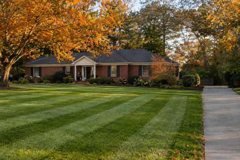 Striped lawn and clean driveway in front of a brick home in fall